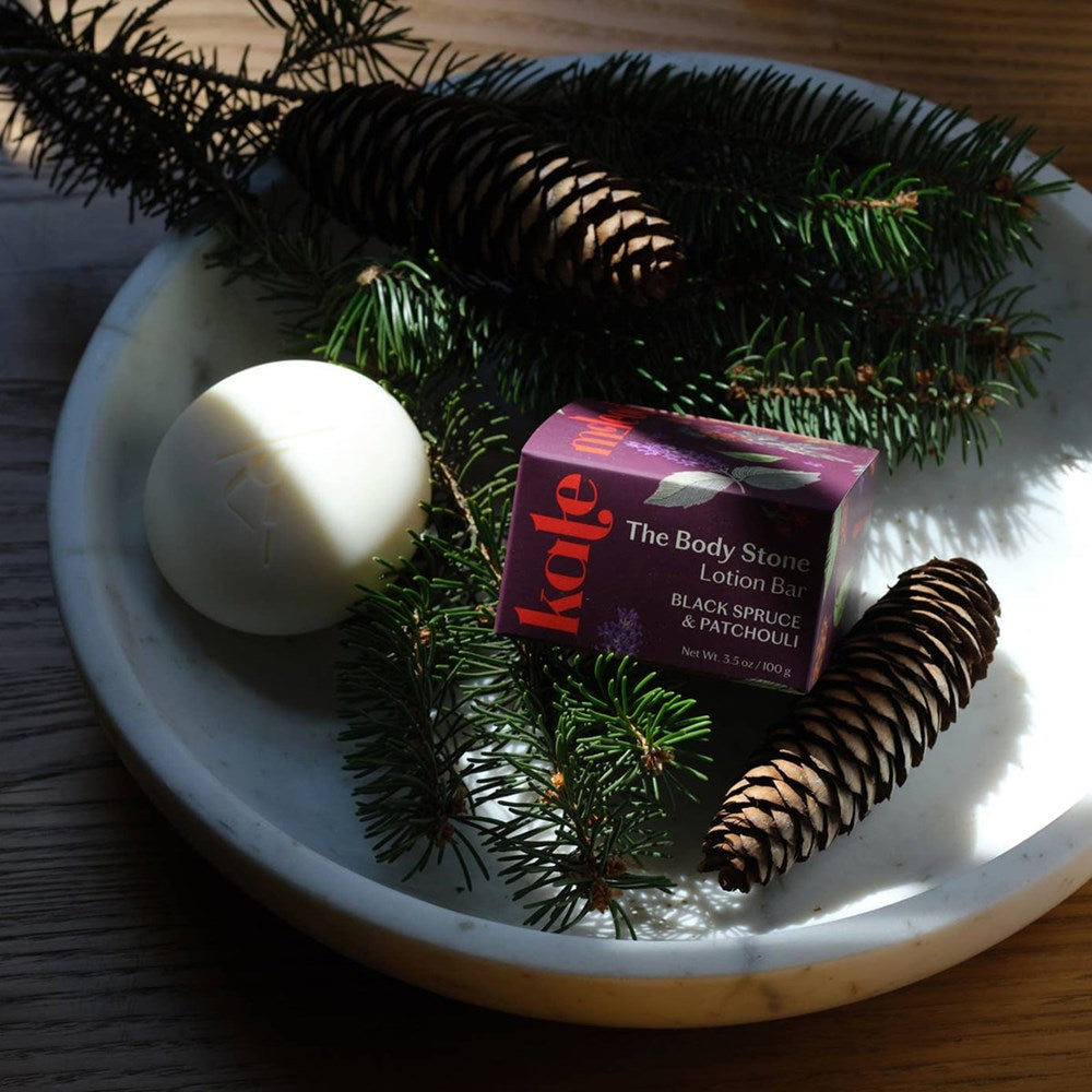Kate McLeod Black Spruce & Patchouli Deep Moisturizing Lotion Bar (3.5 oz) - product shown with pine leaves and pinecones in grey bowl. 