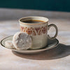 Cup of coffee with a decorative pattern on a saucer, accompanied by two Romero Luna Mexican Wedding Cookies
