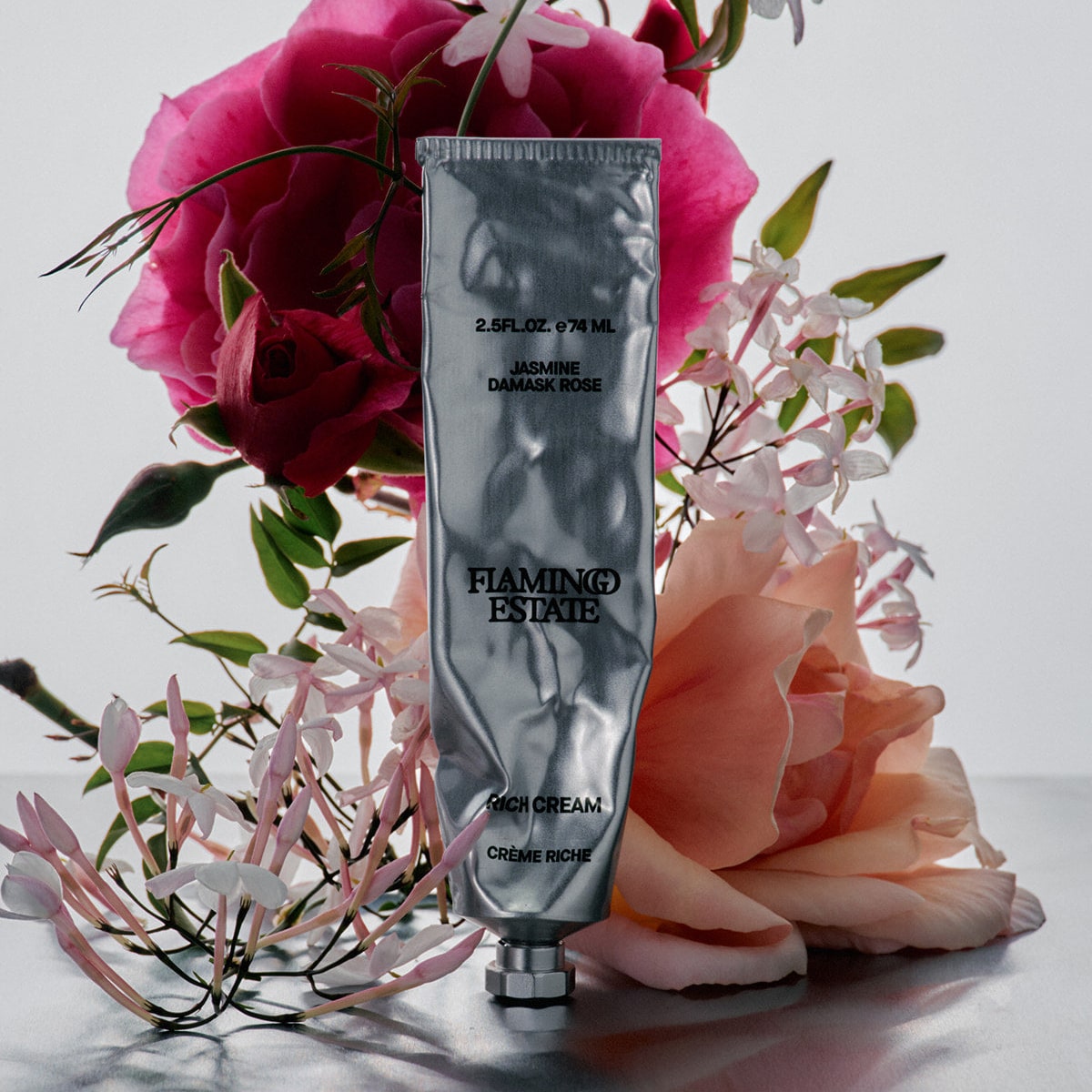 Flamingo Estate Organics Jasmine Damask Rose Rich Cream (74 ml) - product shown against flowers. 
