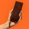 Hand holding aElements Almond Crunch Chocolate Bar (1.8 oz) against an orange background