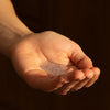 Hand holding a small amount of Naomi After-Cooking Hand Scrub - Bergamot & Black Pepper Hand Wash against a dark background