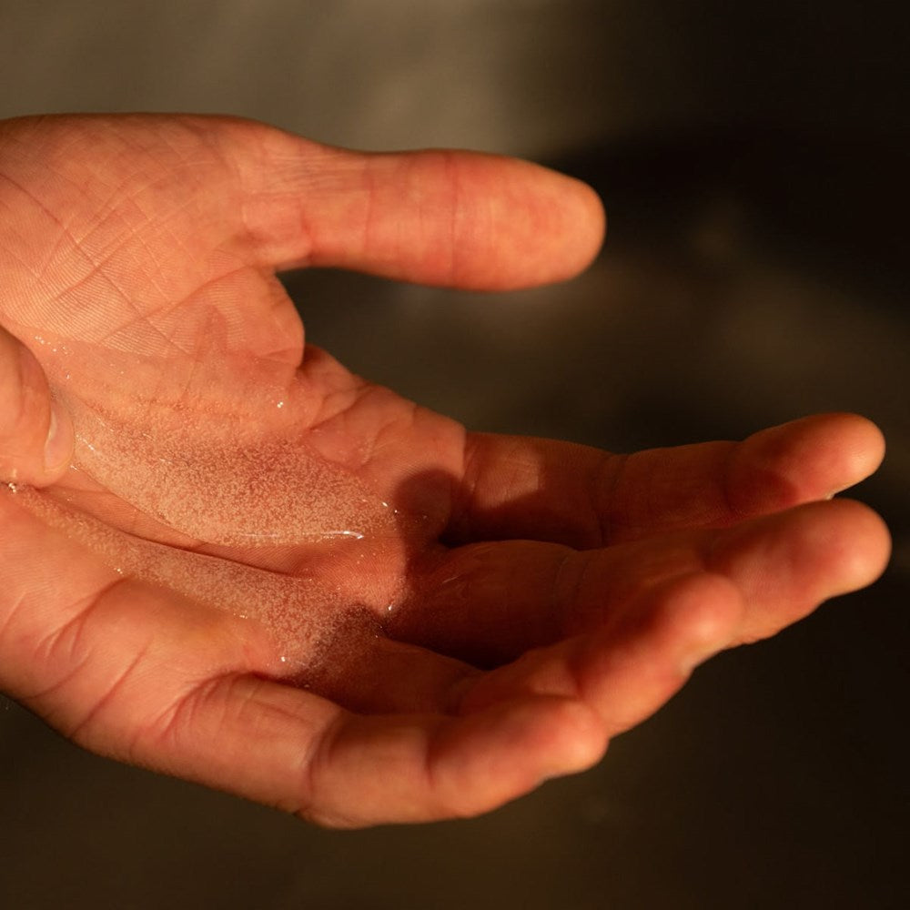 Hand holding Naomi After-Cooking Hand Scrub - Cardamom & Iris Luxury Hand Wash with a dark background