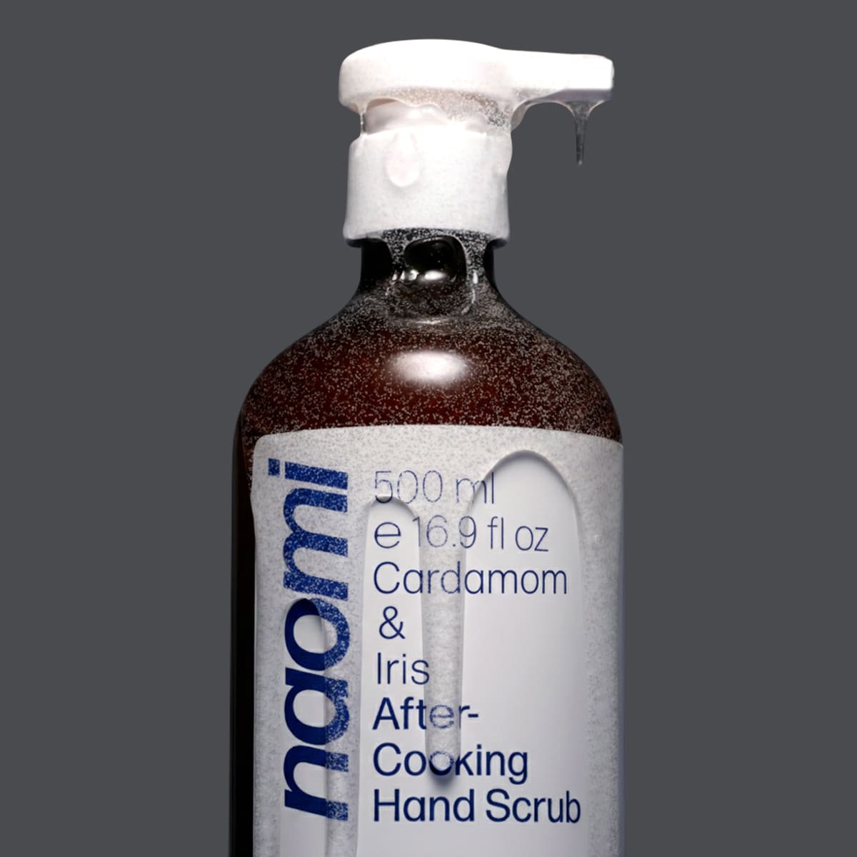 Bottle ofNaomi After-Cooking Hand Scrub - Cardamom & Iris Luxury Hand Wash (500 ml) with scrub falling from pump and on bottle with a gray background