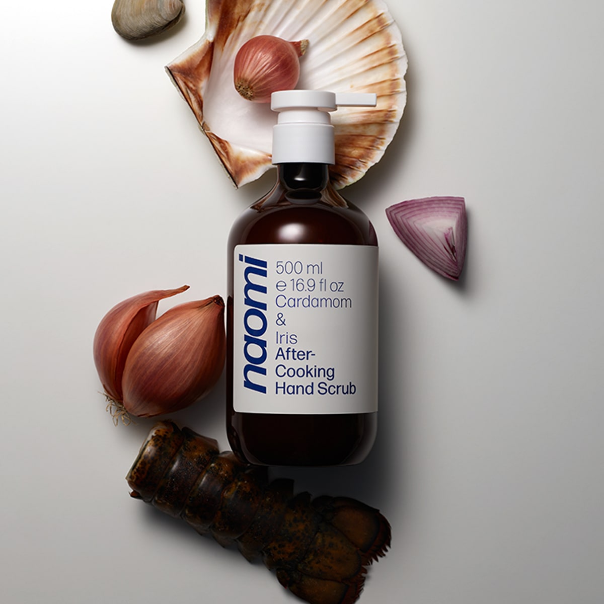 Bottle of Naomi After-Cooking Hand Scrub - Cardamom & Iris Luxury Hand Wash (500 ml) with shellfish, lobster tail and onions in the background