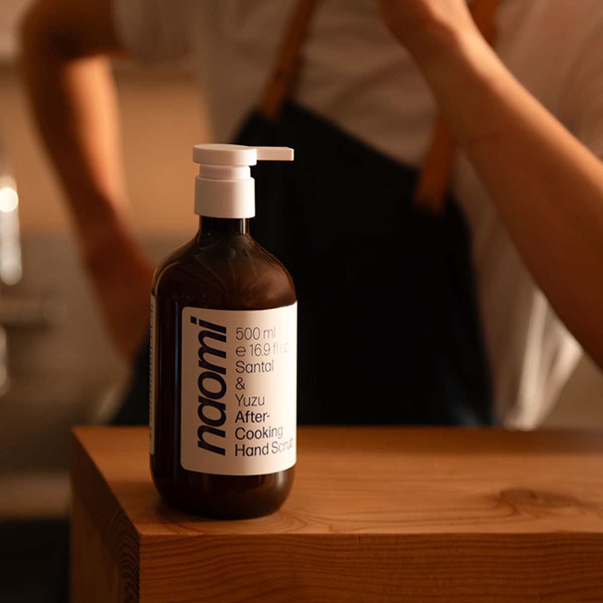 Lifestyle shot of Naomi After-Cooking Hand Scrub - Cardamom & Iris Luxury Hand Wash (500 ml) on wood table with chef in the background
