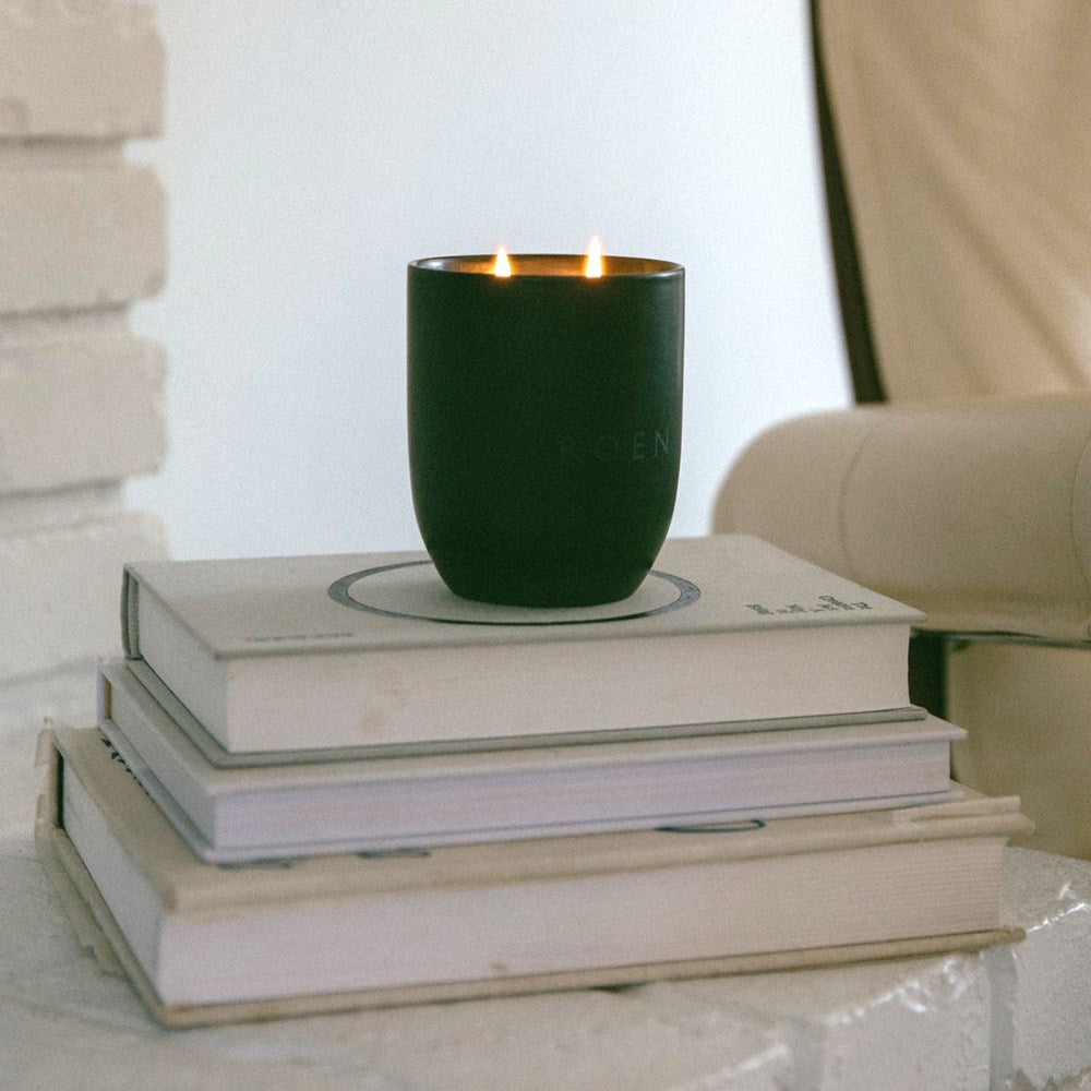 Lifestyle shot of ROEN Candles Sacre Scented Candle (14 oz) burning on a stack of books