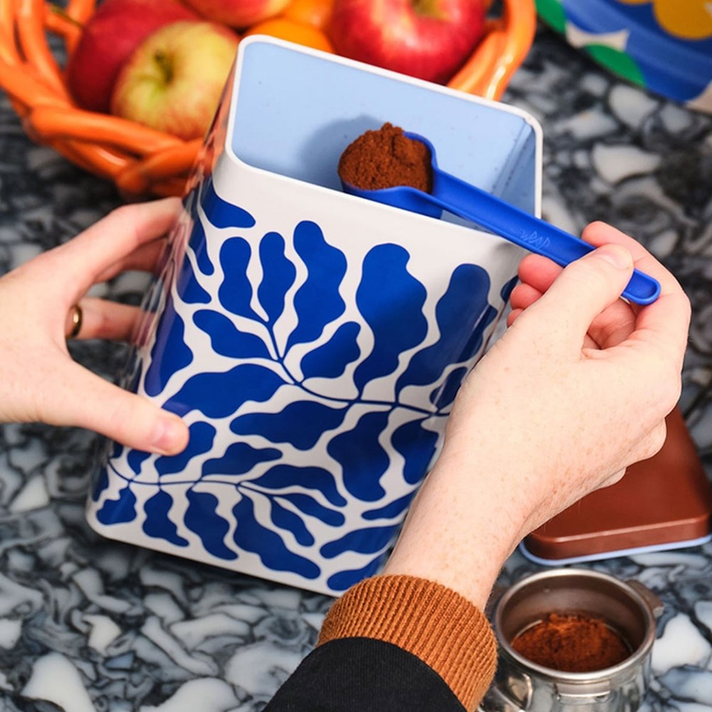 Person using Wrap Leaves Coffee Tin (2 pcs) with a scoop to measure coffee grounds. Coffee not included.