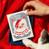 Bromstad Printing Co. You are Iconic Risograph Greeting Card (1 pc) - product shown on red cloth and blue tray with cat paw. 