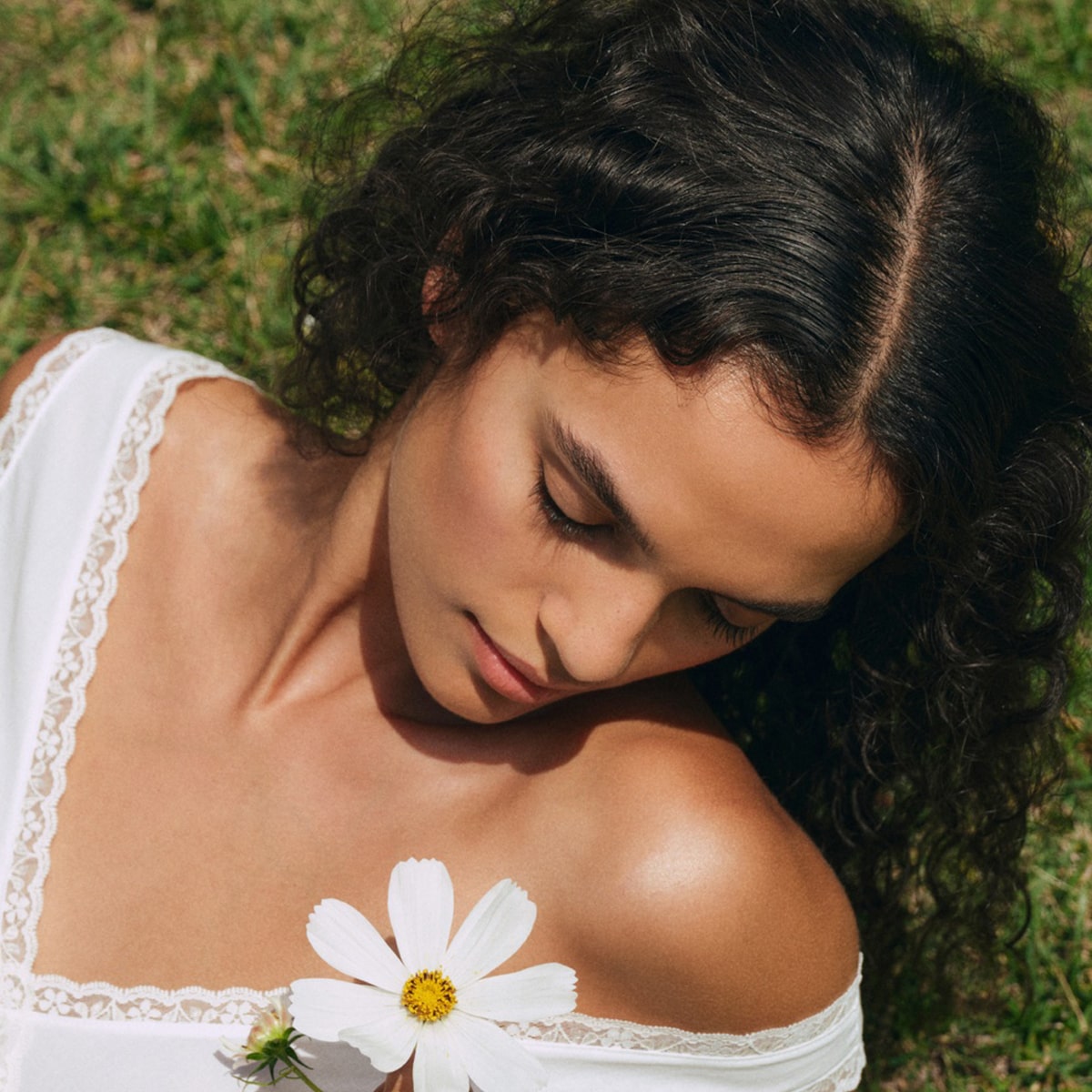Roz SALT Scalp Scrub (200 ml) - model with curly hair looking down at a flower. 