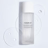 Cosmetics 27 Toner 27 Hydrating and Balancing Skin-Priming Essence Water (100 ml) with product drops in the background
