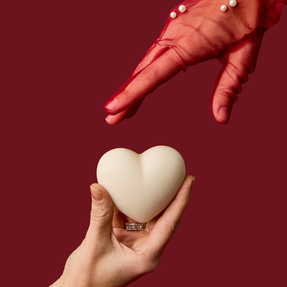 Kate McLeod Spicy Cacao Heart-Shaped Lotion Bar (3.18 oz) - product shown being held on a red background. 