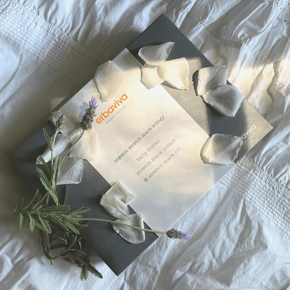 Erbaviva Stretch Mark Trilogy (3 pcs) - product shown on white bedding with flower petals and purple flowers. 