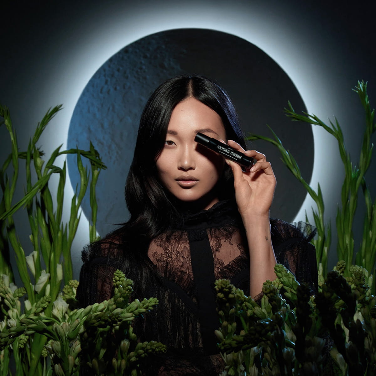 Heretic Parfum Nocturnal Tuberose Eau de Parfum (15 ml) - product shown being held by model with plants and moon.