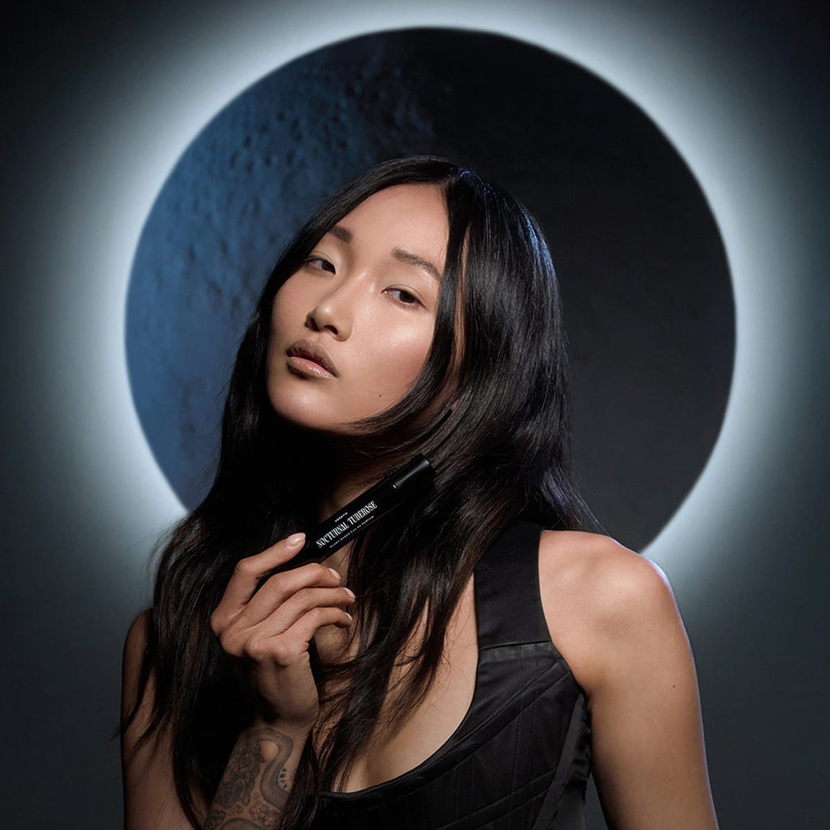 Heretic Parfum Nocturnal Tuberose Eau de Parfum (15 ml) - model shown holding product with moon in the background. 