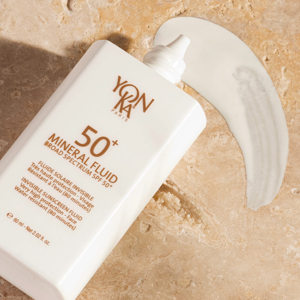 Yon-Ka Paris 50+ Mineral Fluid Broad Spectrum Sunscreen (60 ml) - product shown on counter with swatch underneath it. 