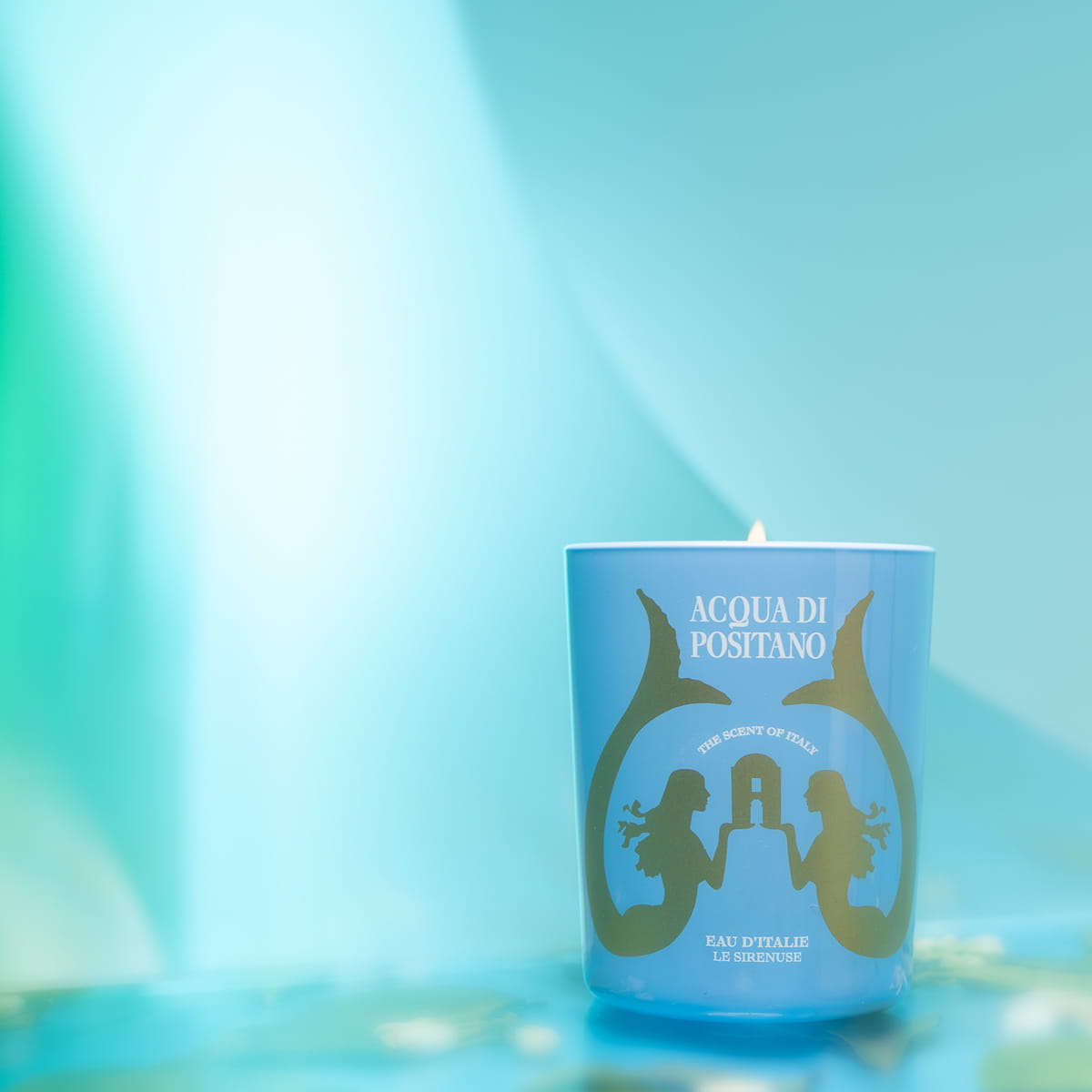 Eau d'Italie Acqua Di Positano Candle (6.5 oz)  - product shown lit on blue background. 