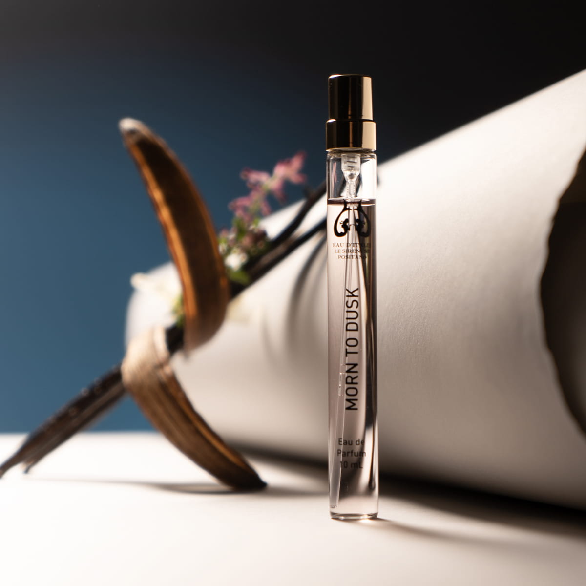 Lifestyle shot of Morn to Dusk Eau de Parfum Spray (10 ml) - product shown in front of papers and flowers.