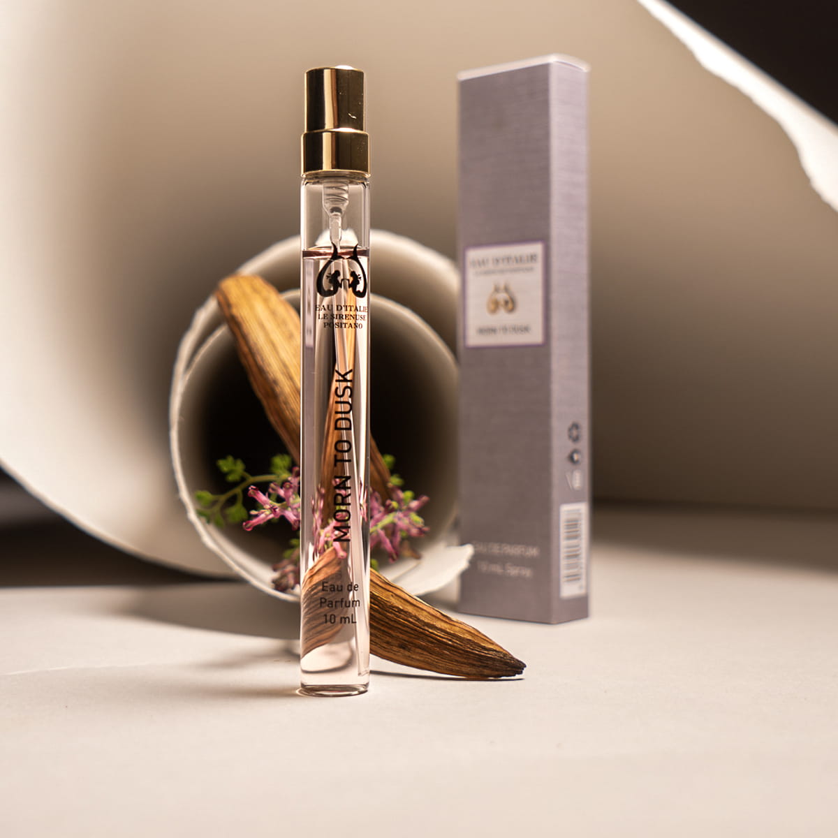 Lifestyle shot of Morn to Dusk Eau de Parfum Spray (10 ml) - product shown in front of papers and flowers. 
