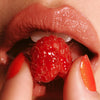 Good Weather Skin Daily Lip Sun Gloss SPF 30 - Ripe Berry (17 g)  - product shown on model who is eating a raspberry.