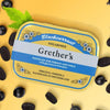 Lifestyle shot of Grether’s Pastilles Blackcurrant Tin - Sugarfree (110 g) with pastilles and mint leaf in the background