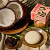 Kate McLeod Tonka Bean & Coconut Deep Moisturizing Lotion Bar (3.5 oz) - product shown on table with packaging and fruits. 