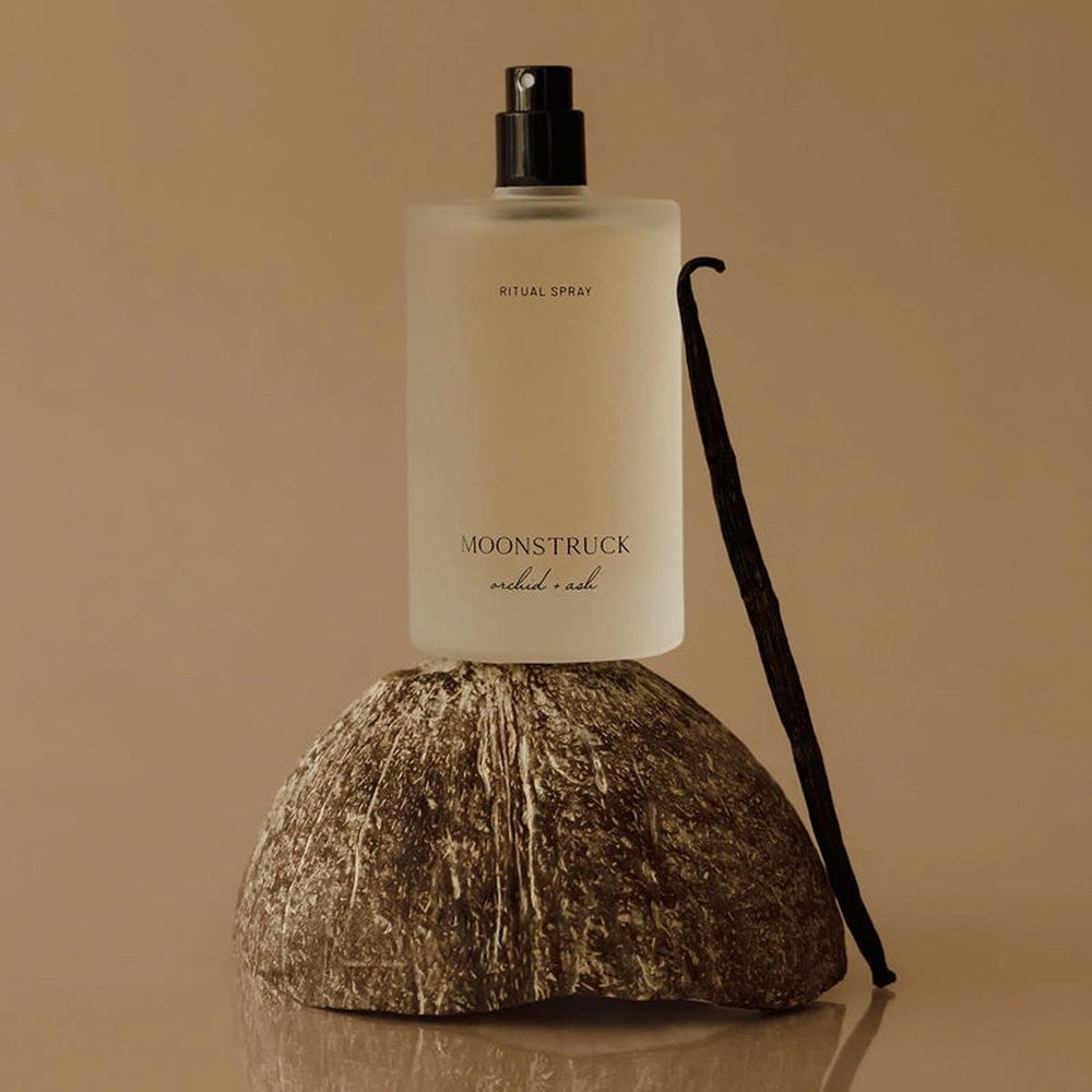 Lifestyle shot of Orchid + Ash Moonstruck Ritual Spray (100 ml) on a coconut shell with a vanilla bean pod against a beige background