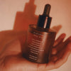 Mari Body Midsummer All-Over Oil (50 ml) - product shown being held by a hand. 