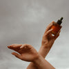 Mari Body Midsummer All-Over Oil (50 ml) - product shown being held in front of a cloudy sky. 