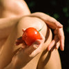 Person holding a red tomato with a bite in it against their skin outdoors