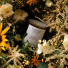Lifestyle shot of Flamingo Estate Organics Golden Pollinator Candle (226 g) with flowers in the background