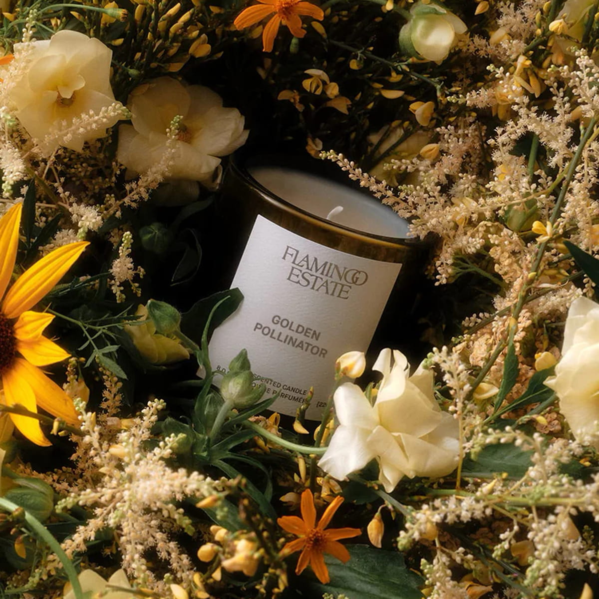 Lifestyle shot of Flamingo Estate Organics Golden Pollinator Candle (226 g) with flowers in the background