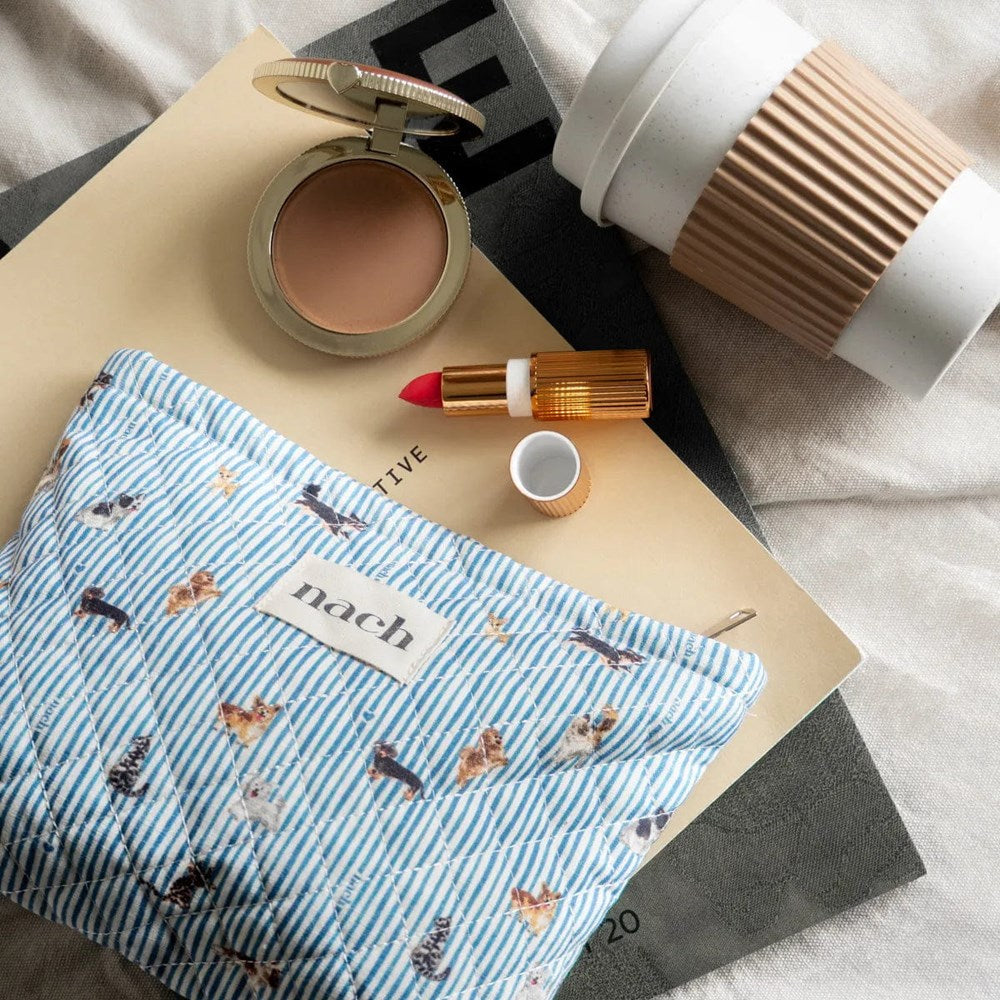 Nach Cats & Dogs Quilted Striped Pouch (1 pc) - product shown on top of magazines next to lipstick, coffee, and blush. 