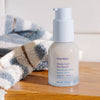 Ursa Major Sunny Start Eye Serum (0.5 oz) on a wood table with a stripped towel in the background