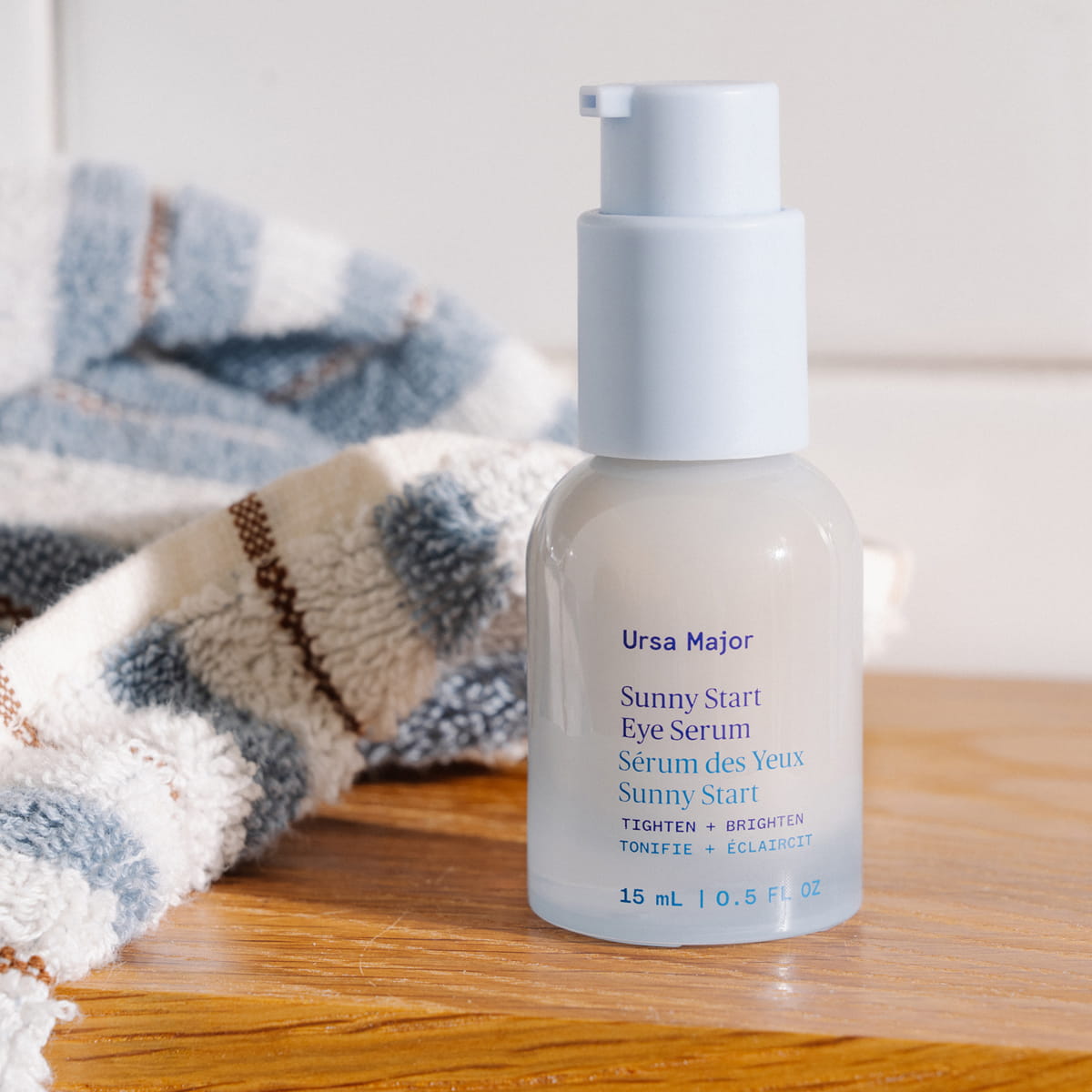 Ursa Major Sunny Start Eye Serum (0.5 oz) on a wood table with a stripped towel in the background