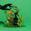 Heretic Parfum The Entomologist Insect Repellent Spray (200 ml) - product shown on green background with flowers and a gloved hand. 
