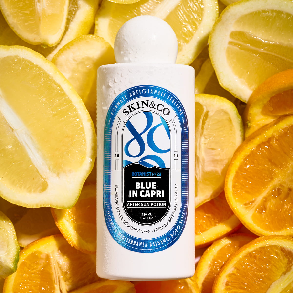 Skin & Co Blue in Capri After Sun Potion (250 ml) with lemons and oranges in the background