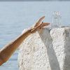 See You Sundae Clear Tanning Water (100 ml) - product shown on rock at beach. 