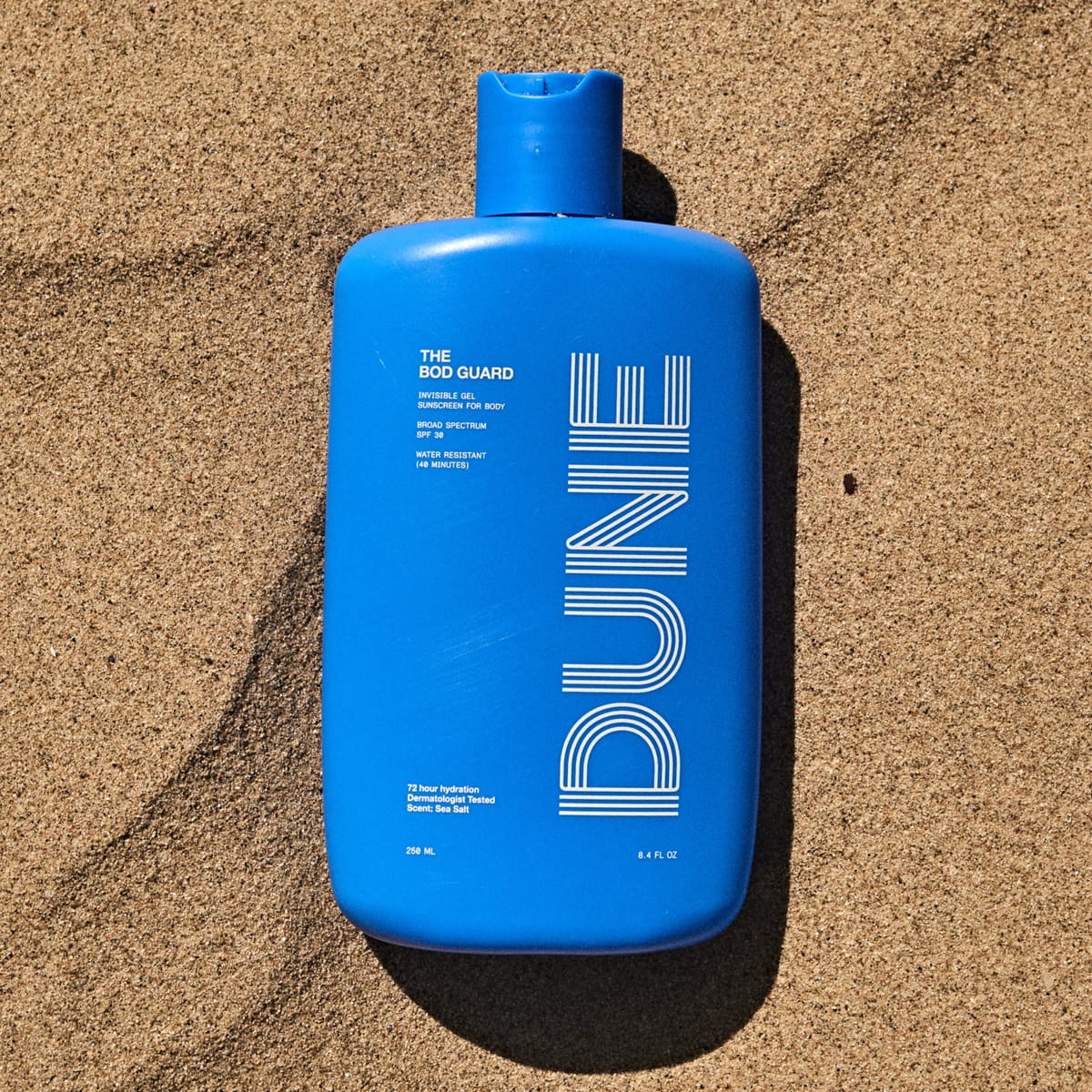 DUNE Suncare The Bod Guard (250 ml) - product shown in sand. 