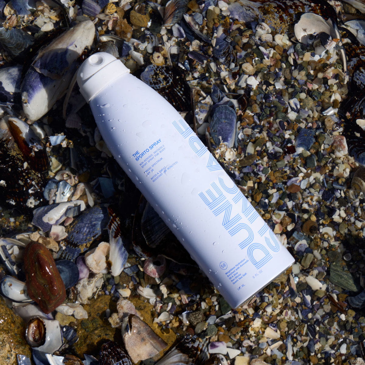 DUNE Suncare The Sporto Spray (148 ml) - product shown on top of shells.