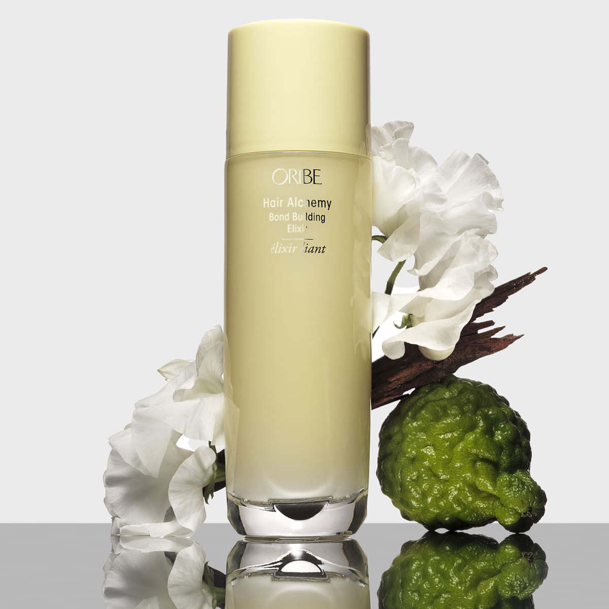 Oribe Hair Alchemy Bond Building Elixir (3.4 oz) - product shown with flowers and fruit. 