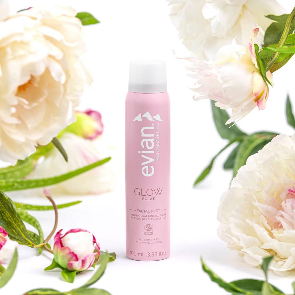 Evian Glow Facial Mist (100 ml) - product shown surrounded by flowers.