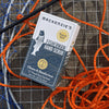 Lifestyle shot of a box of Mackenzie's Fisherman Hand Scrub with bright orange and blue ropes and fisherman's net in the background