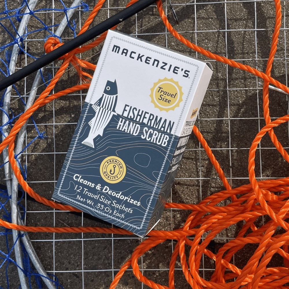Lifestyle shot of a box of Mackenzie's Fisherman Hand Scrub with bright orange and blue ropes and fisherman's net in the background