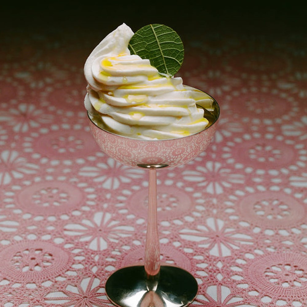 A dessert in metal champagne glass topped with a small green leaf and drizzled with Flamingo Estate Fennel Flower Infused Extra Virgin Olive Oil (222 ml) set on a pink lace doily.