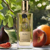 Lifestyle shot of Parfums de Nicolai Fig Tea Intense (100 ml) shown outdoors among green leaves, with a fig, peach, and orange in the background