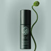 Lifestyle shot of Roz Milk Styling Mousse (150 ml) with a green plant stem and seed pod against a light green background.
