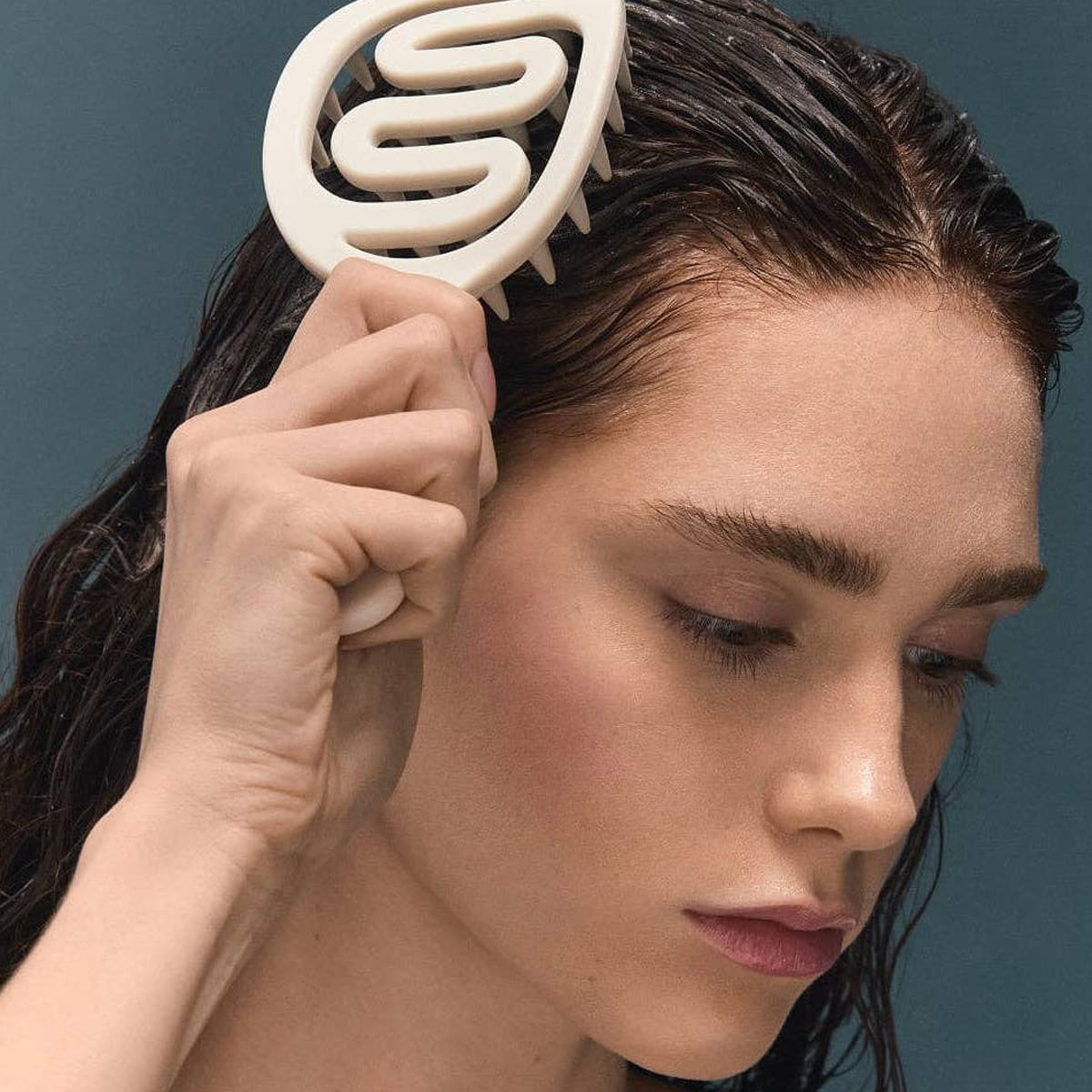 A close-up lifestyle shot of a woman with wet dark hair using BASE-K The Scalp Massager Stimulating Silicone Scalp Brush