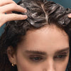 Close-up of woman applying BASE-K The Rice Powder Detox Micro-Exfoliating Scalp Scaling Shampoo to the roots and scalp.