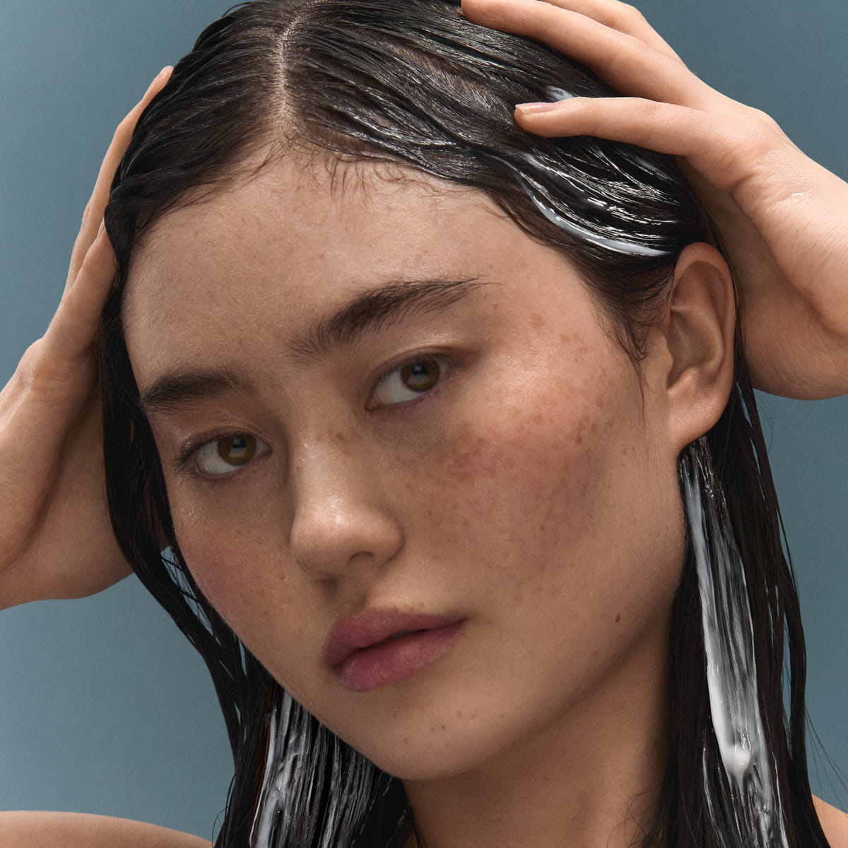 Close-up of a woman with wet dark hair applying BASE-K The Rice Cream Thickening Conditioner to hair