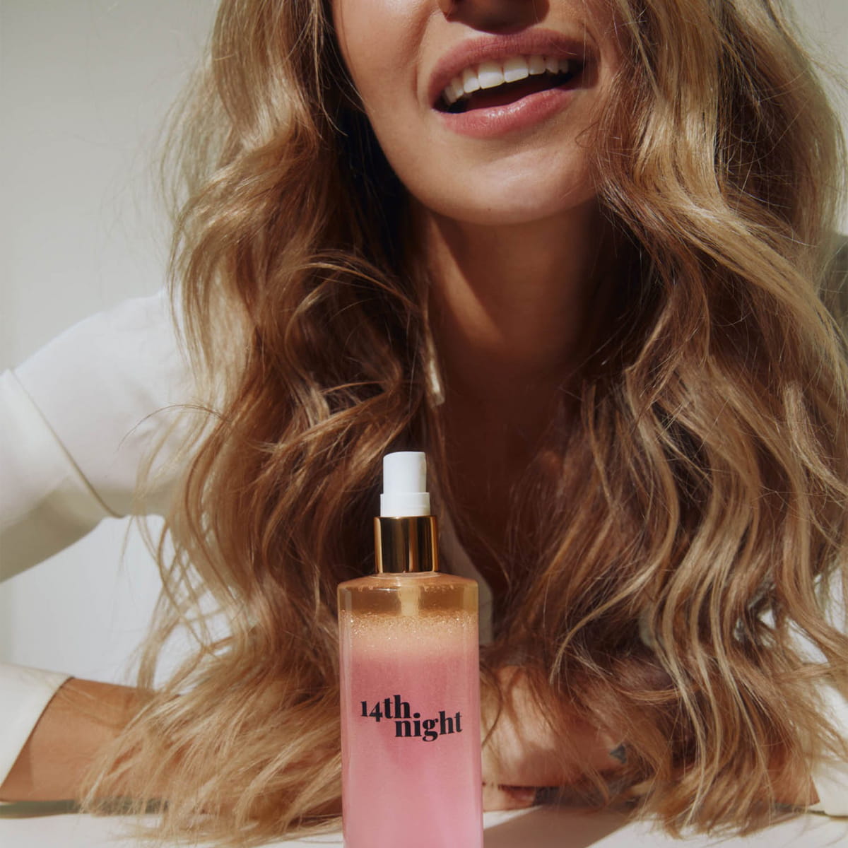A woman with long wavy blonde hair with 14th Night Natural Surf Spray in front of her